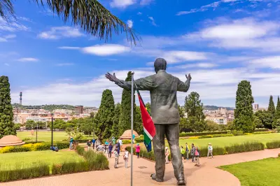 The Nelson Mandela statue at the Union Buildings overlooks Pretoria, with visitors, formal gardens and the South African flag visible below.
