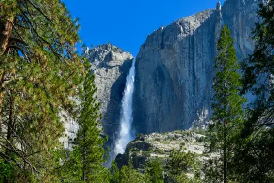 Yosemite Falls cascading down a granite cliff in Yosemite Valley, California, surrounded by pine trees in spring.