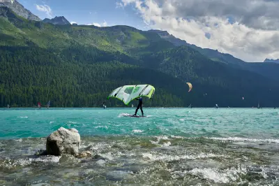 Wing surfer and kiteboarders on turquoise Lake Silvaplana with alpine forest and mountains in the Engadin, Switzerland