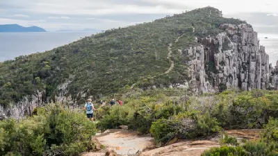 Hikers on the walking track beside towering dolerite cliffs at Cape Hauy, Tasmania.