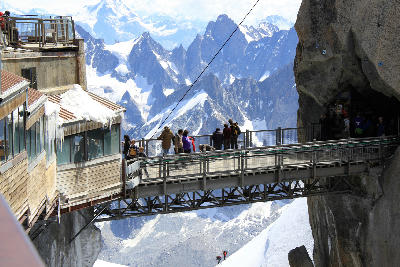 Visitors on the Aiguille du Midi bridge above steep alpine terrain in the Mont Blanc Massif.