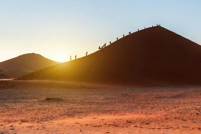 People silhouetted against sunrise while climbing Dune 45 in the Sossusvlei region of Namibia.