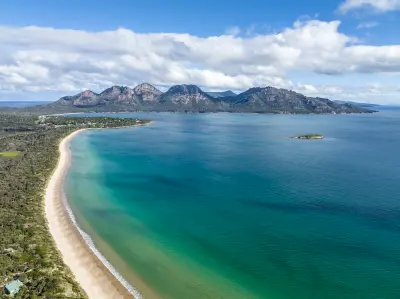 Aerial view across Muirs Beach and Great Oyster Bay toward the rugged granite peaks of The Hazards near Coles Bay, Tasmania.