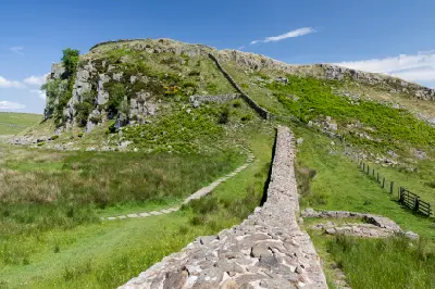 Hadrian's Wall ascending a steep grassy and rocky hillside at Peel Crags near Steel Rigg, Northumberland, England, beneath a blue sky.