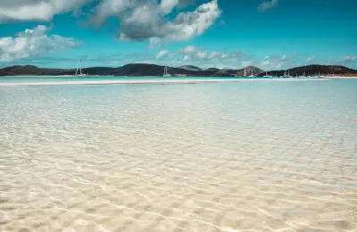Clear shallow water over white silica sand with yachts offshore at Whitehaven Beach, Queensland, Australia.