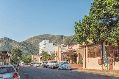 Street scene in Barberton with historic buildings, parked vehicles and the Makhonjwa Mountains rising behind the town.