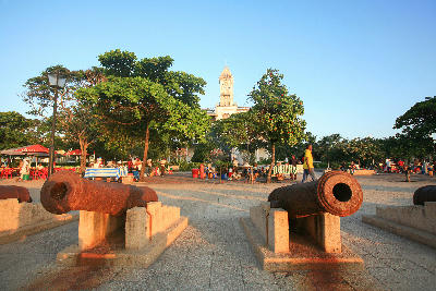Historic cannons facing Forodhani Gardens with food stalls and the Old Fort clock tower in the background, Stone Town, Zanzibar.