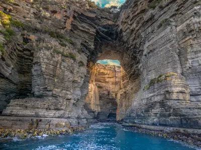 Sea-level view through Tasman Arch surrounded by towering layered cliffs on the Tasman Peninsula, Tasmania.