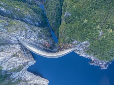 Top-down aerial view of the curved Gordon Dam, Lake Gordon and the narrow forested gorge in southwest Tasmania, Australia.