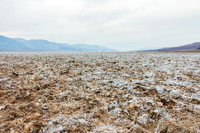 Rough salt formations across Badwater Basin under overcast skies with the Panamint Mountains in the distance, Death Valley National Park, California.