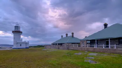 White Point Perpendicular Lighthouse beside the historic keeper’s quarters beneath dramatic purple-grey clouds at dusk.