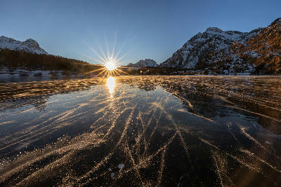 Frozen Lake Sils with ice patterns and sunburst at sunset, Engadin, Switzerland.