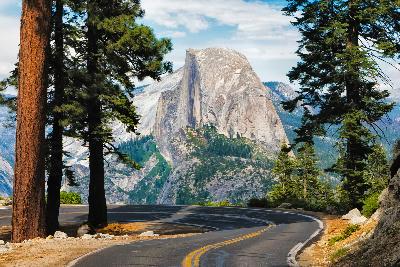 Curving road to Glacier Point Yosemite with Half Dome granite dome framed by pine trees in the background.