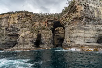 Sea-level view of Tasman Arch within towering layered coastal cliffs on the Tasman Peninsula, Tasmania.