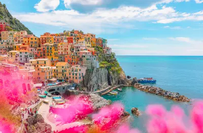 Summer landscape of Manarola in Cinque Terre, with colourful buildings, pink flowers in the foreground, and a blue sky with scattered clouds, Italy.