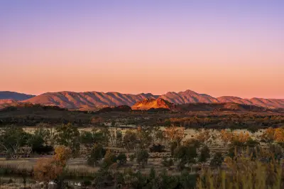Sunset light illuminates the ridges of the West MacDonnell Ranges above the Central Australian landscape.