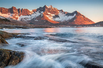 Rocky shoreline with flowing water looking across Mefjorden toward snow-covered mountains