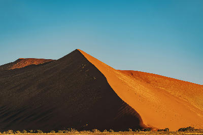 Sunlit crest and deep shadow on Dune 45 in the Sossusvlei desert of Namibia beneath a clear blue sky.