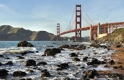 Golden Gate Bridge viewed from Baker Beach with rocky shoreline and waves breaking along the coast