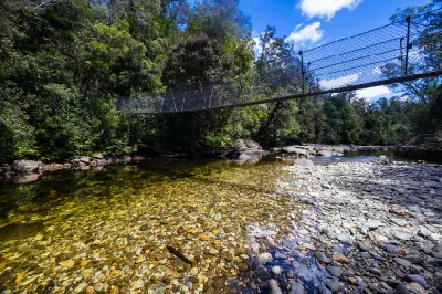 Suspension bridge above a clear rocky river on the Frenchmans Cap Track in Tasmania.