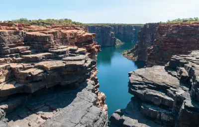 View from above King George Falls along the deep blue King George River, enclosed by towering layered sandstone cliffs.