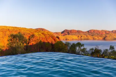 Infinity pool overlooking Lake Argyle and its rugged red hills illuminated by warm sunset light.