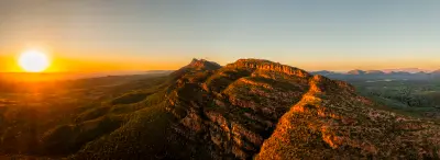 Aerial sunset view of Wilpena Pound's sandstone ridges and mountain peaks glowing orange in the Flinders Ranges, South Australia.