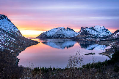 Bergsbotn viewpoint Senja Norway overlooking Bergsfjord with still reflective water and snow covered mountains at sunset.