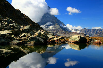 Matterhorn partially covered by clouds reflected in Riffelsee with foreground rocks and clear alpine water, Zermatt, Switzerland.