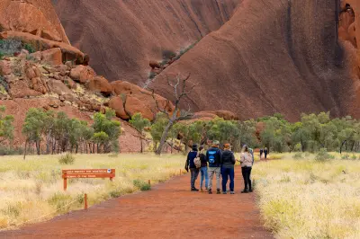 Visitors walking along a marked trail beneath the sandstone walls of Uluru in Uluru-Kata Tjuta National Park, Australia.