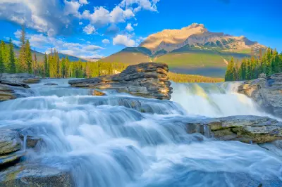 Athabasca Falls cascading over layered rock with forest and mountain backdrop along the Icefields Parkway, Jasper National Park, Canada