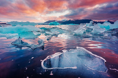 Icebergs floating in Jökulsárlón Glacier Lagoon on Iceland’s South Coast at sunset, with colorful clouds reflected in the water and distant mountains in the background.