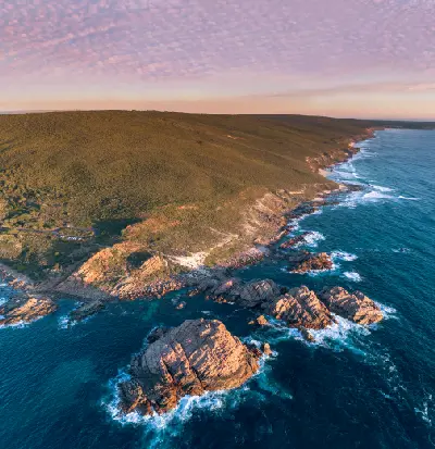 Aerial view of Sugarloaf Rock surrounded by deep blue ocean and breaking surf along Western Australia’s rugged Margaret River coast.