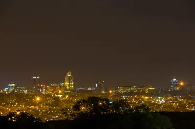 Night view of the Sandton skyline in Johannesburg, South Africa, with illuminated high-rise buildings and city lights under a dark sky.
