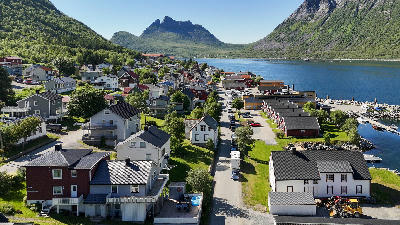 Aerial view of Gryllefjord village on Senja showing houses, harbour, and fjord framed by steep green mountains