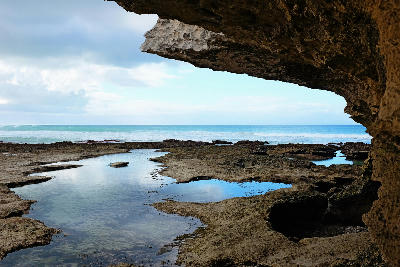 Rock overhang framing tidal pools and the ocean at Waenhuiskrans Cave near Arniston in the Western Cape, South Africa.