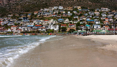 Fish Hoek Beach with small waves, sandy shoreline, and hillside houses along False Bay in Cape Town, South Africa.