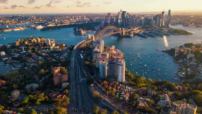 Aerial view across Sydney Harbour with the Harbour Bridge, Opera House, city skyline and boats in warm late-afternoon light.