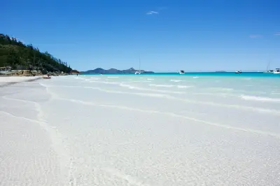 Shallow clear water over white silica sand at Whitehaven Beach with boats anchored offshore, Whitsunday Island, Queensland.