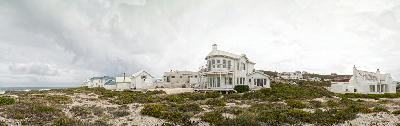 Beachfront homes surrounded by coastal dunes and indigenous vegetation beneath dramatic storm clouds near Yzerfontein, South Africa.