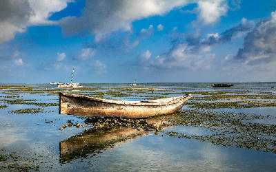 Traditional wooden dhow boat at low tide on Jambiani Beach with shallow tidal flats and reflections, Zanzibar, Tanzania.