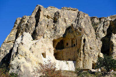 Exterior view of the Dark Church at Göreme Open Air Museum in Cappadocia, Turkey, carved into volcanic rock cliffs beneath a clear blue sky.