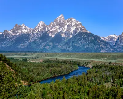 Snake River winding through dense forest with the Teton Range in clear conditions, viewed from Snake River Overlook, Grand Teton National Park, Wyoming.