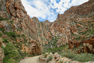 Gravel mountain road passing through towering folded sandstone cliffs in Swartberg Pass in the Klein Karoo of South Africa.