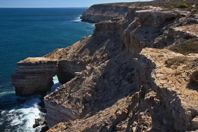 Natural Bridge beneath layered sandstone cliffs along the rugged Kalbarri coastline.