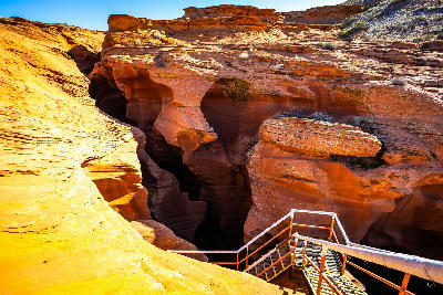 Staircase entrance into Lower Antelope Canyon in Arizona, showing narrow red sandstone slot canyon walls and descending metal stairs.