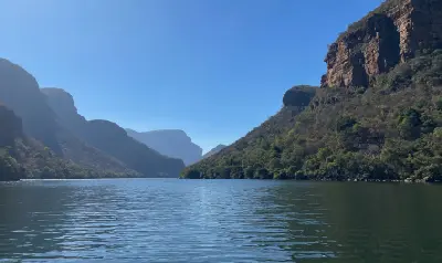 View from a boat on the Blyde River Canyon with calm water, forested canyon slopes, towering sandstone cliffs and distant mountain ridges in Mpumalanga, South Africa.