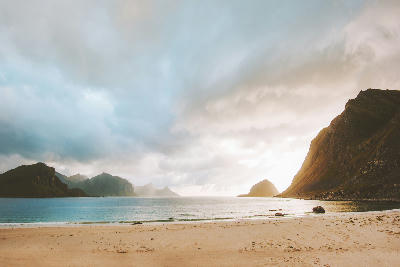 Evening light at Haukland Beach on Vestvågøya in the Lofoten Islands, showing sandy shoreline, calm sea and steep mountains beneath dramatic clouds in Norway.