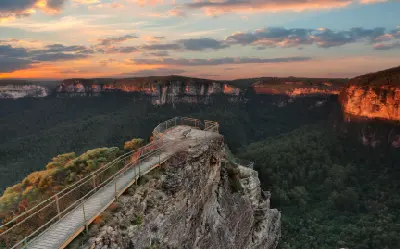 Pulpit Rock’s narrow lookout platform extends above the forested Grose Valley as warm sunrise light illuminates the surrounding sandstone cliffs.
