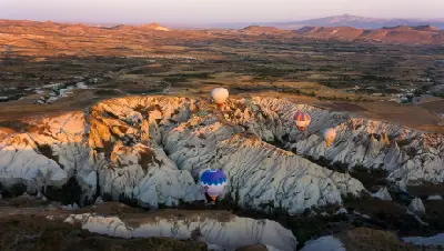 Hot air balloons flying over the white volcanic rock formations of White Valley at sunrise in Cappadocia, Turkey.